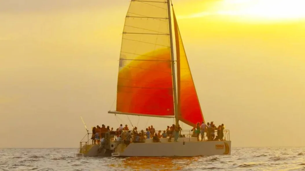 The catamaran silhouetted under a glowing sunset sky off Waikiki